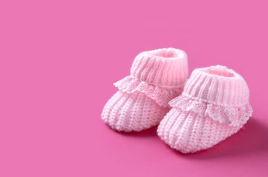 Pink knitted baby booties on a pink background.